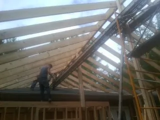 Rafters going up over a new addition with a worker on the wall in Clark