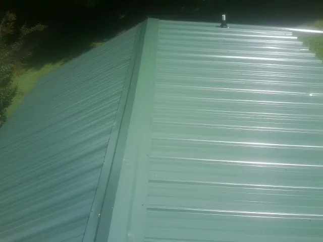 New green metal panels meeting at the ridge of a roof — Flat Roof Repair work by our crew in Clark