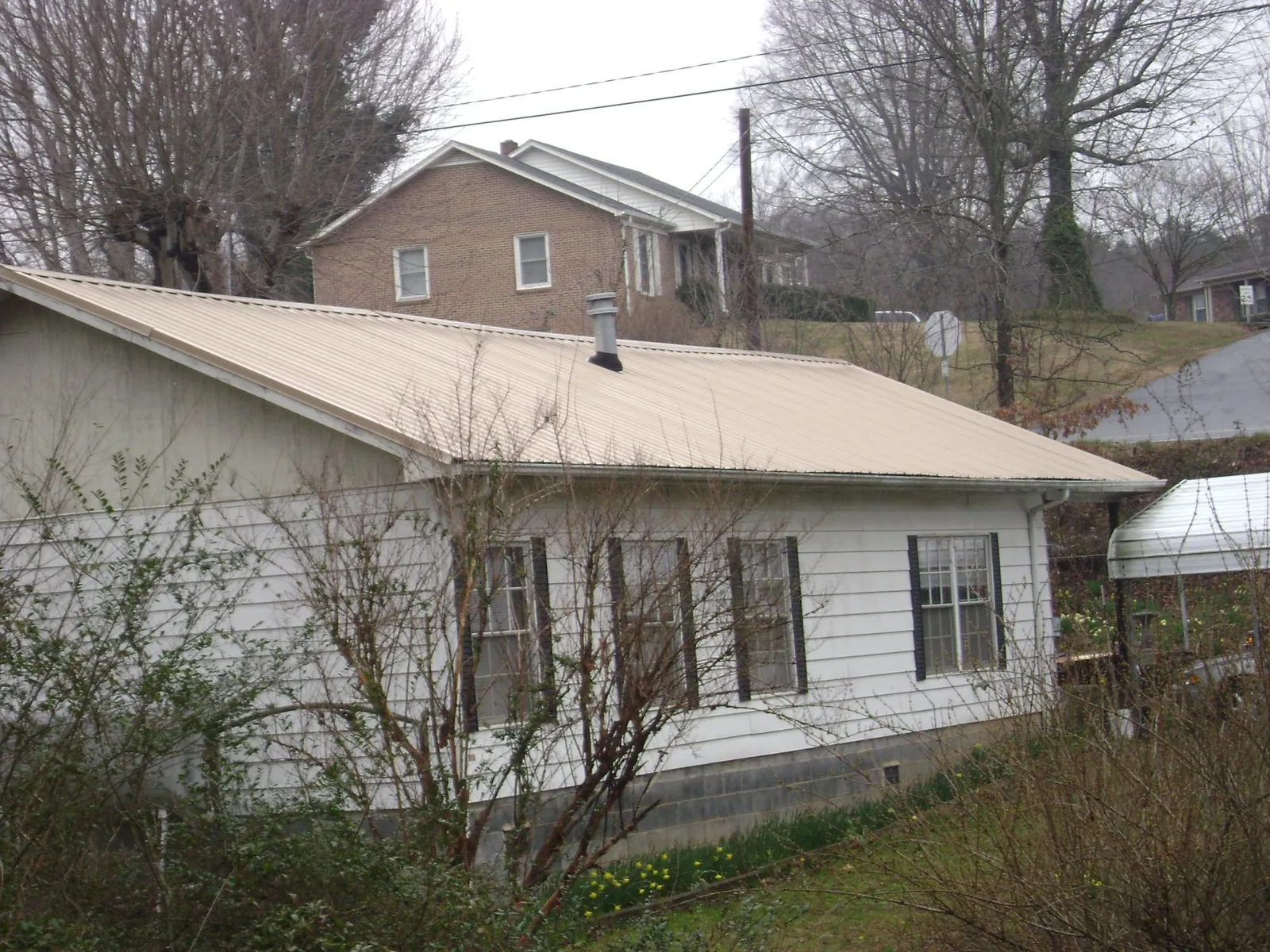 Tan metal roof on a white sided house set into a hillside — Commercial Roofing by Roofing Brothers in Clark